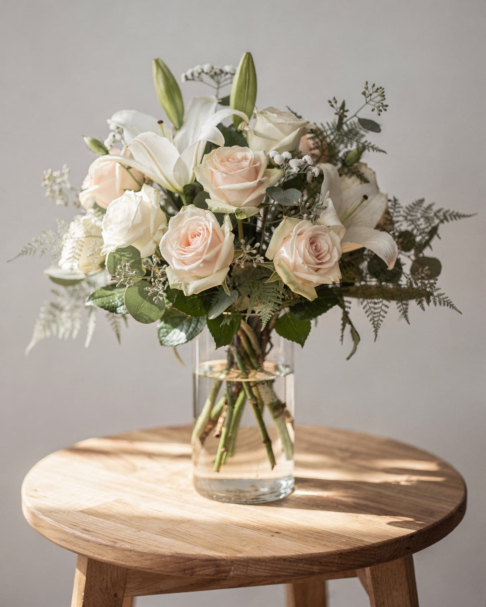 Blush and white roses with white lilies and greenery in a clear glass vase