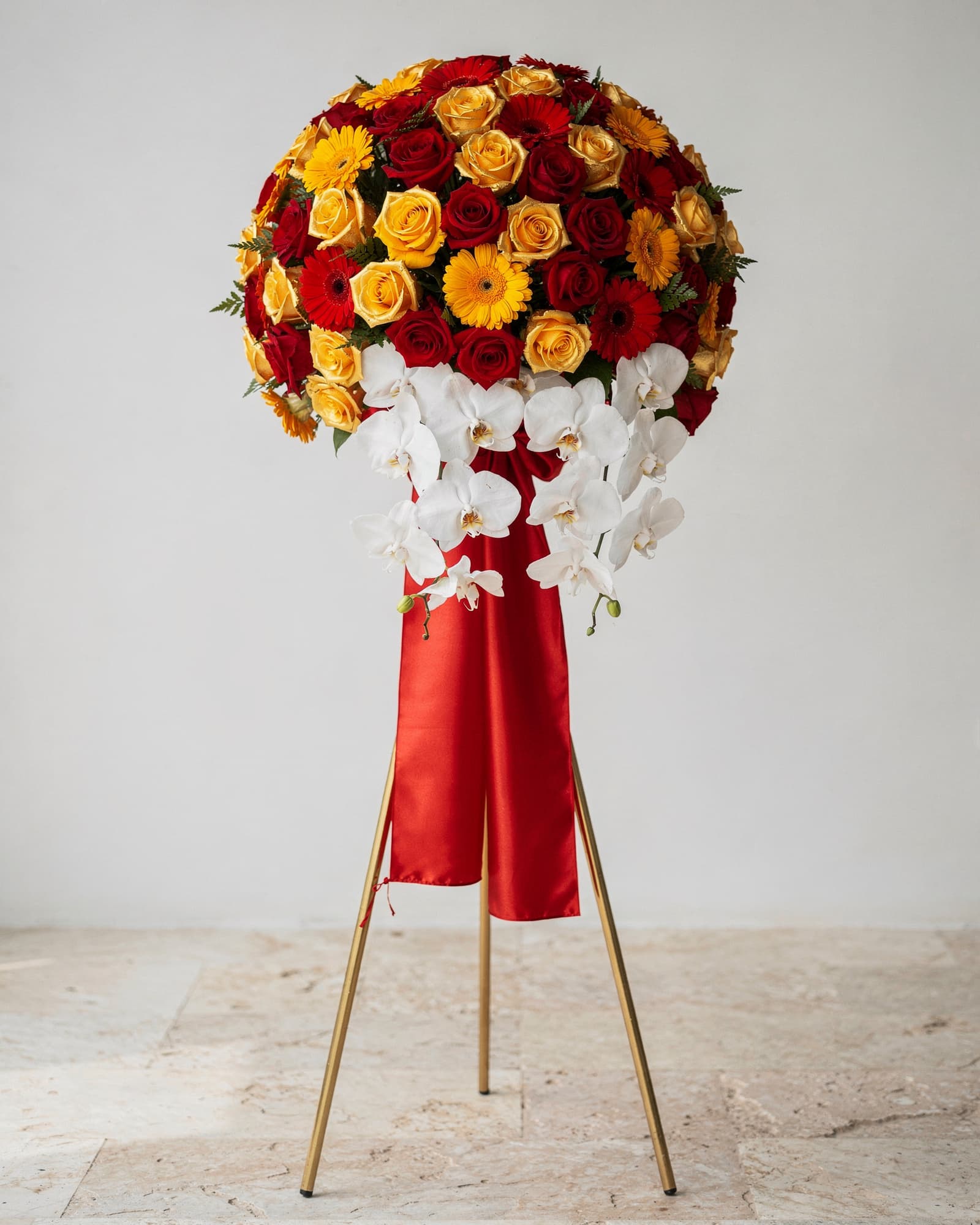 A grand-opening flower stand of red and yellow roses and white orchids on a gold tripod with a red sash